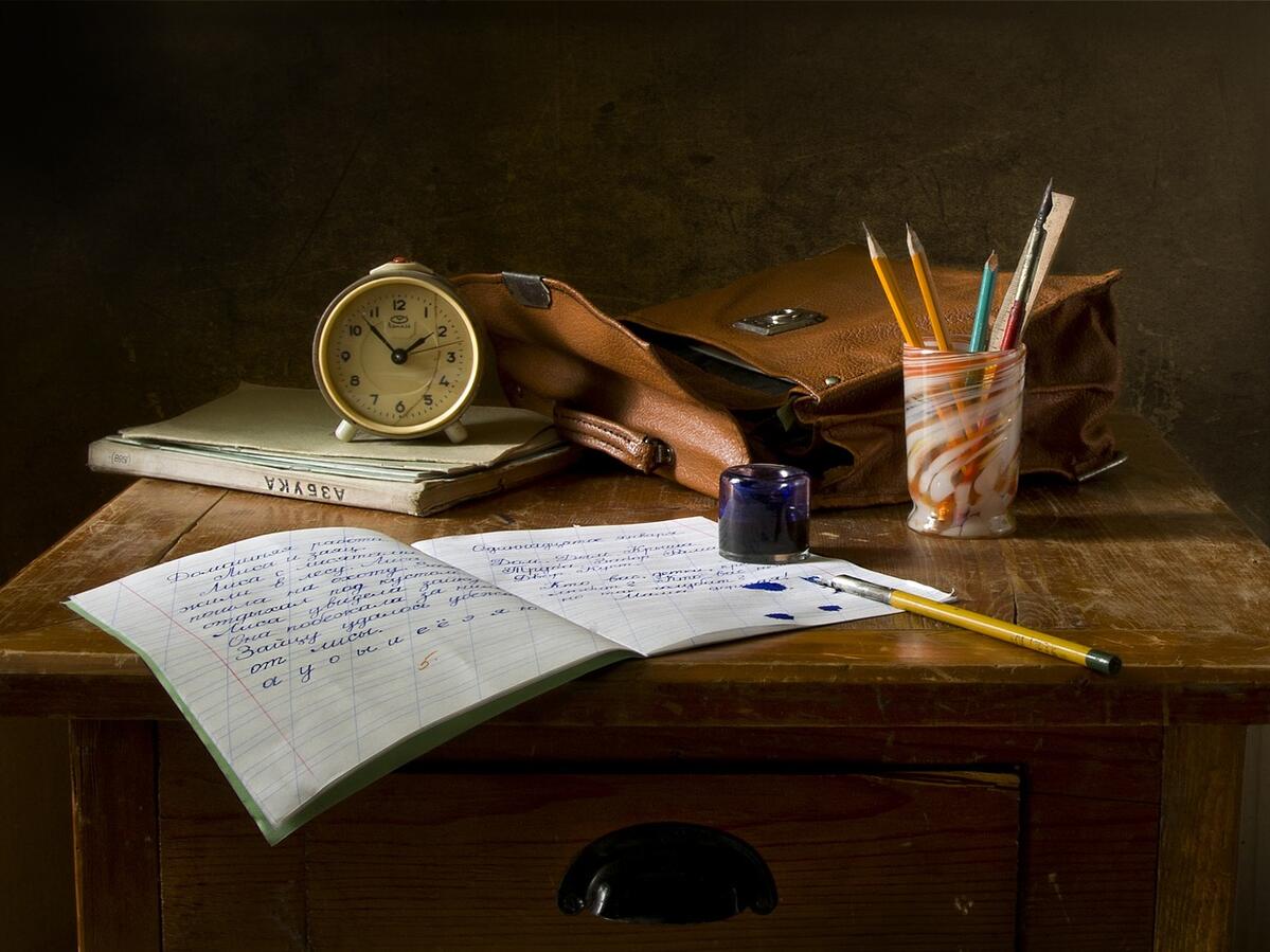 A school desk with a clock, papers, pens and pencils on it
