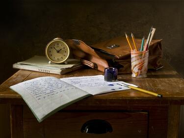 A school desk with a clock, papers, pens and pencils on it